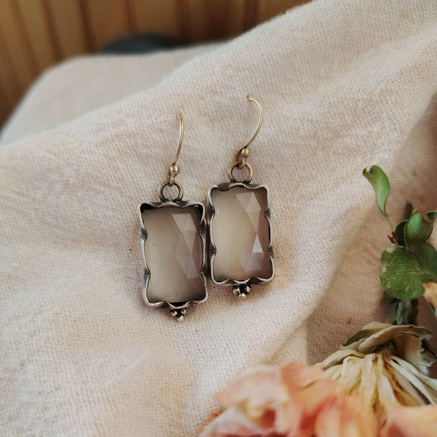 Pair of silver earrings with a beige stone on a beige fabric background with flowers.